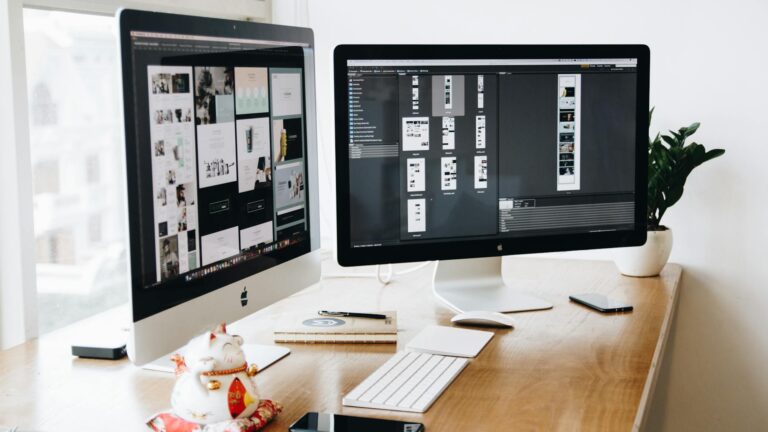 two imac s with keyboard and phones on desk