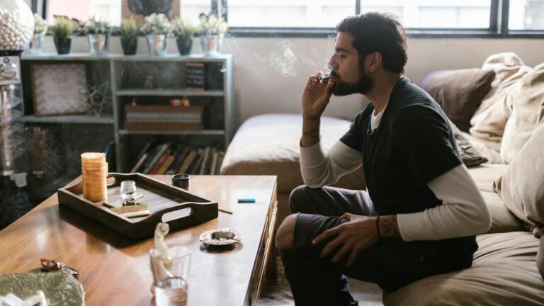 a bearded man sitting on the couch while smoking weed